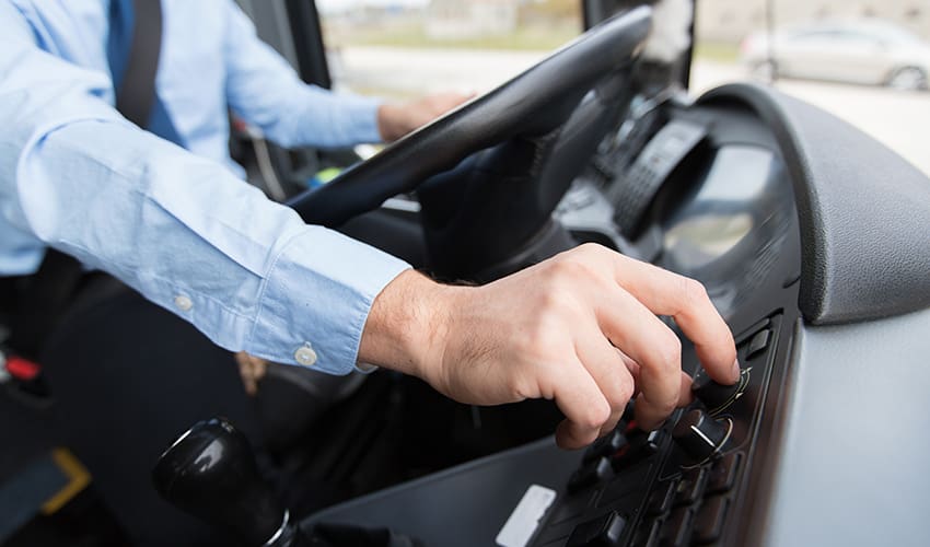 A bus driver at the wheel of a charter bus configures knobs and dials