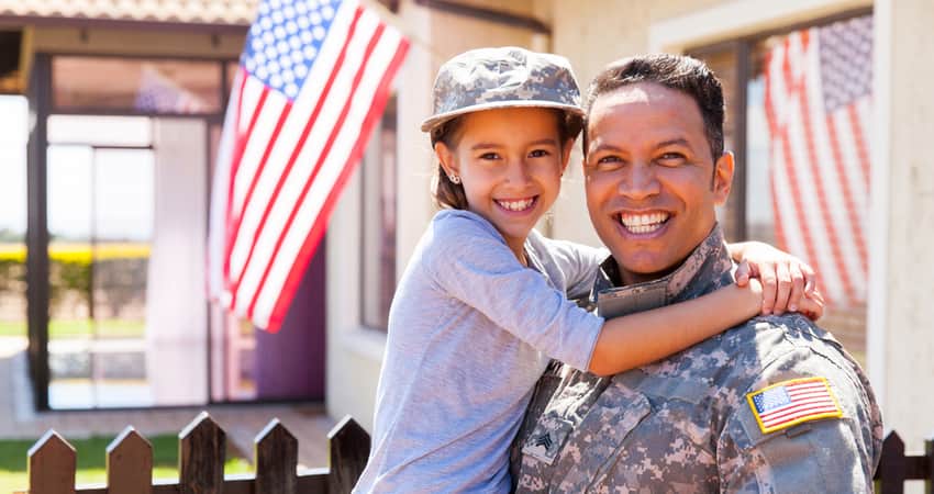 A soldier holding his daughter in front of home