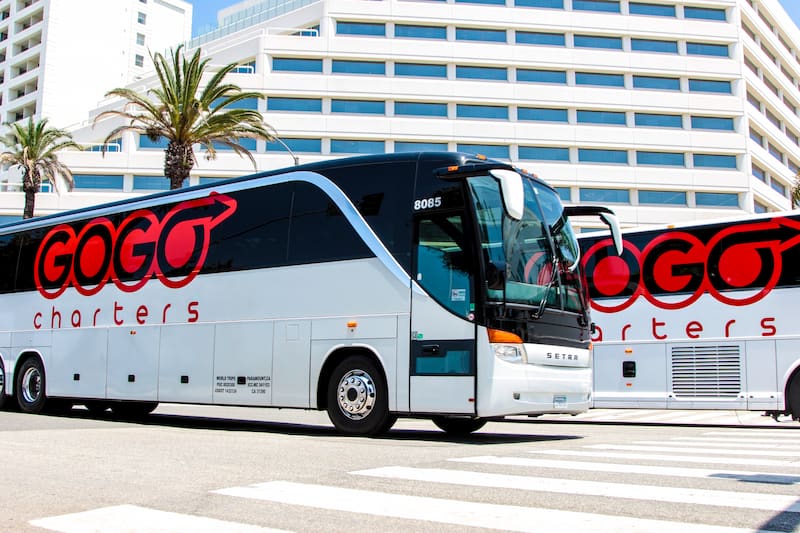 a white charter bus with a gogo charters logo parked outside of a large building