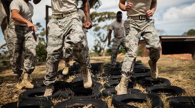 army members in camouflage-print pants run drills through tires on the ground