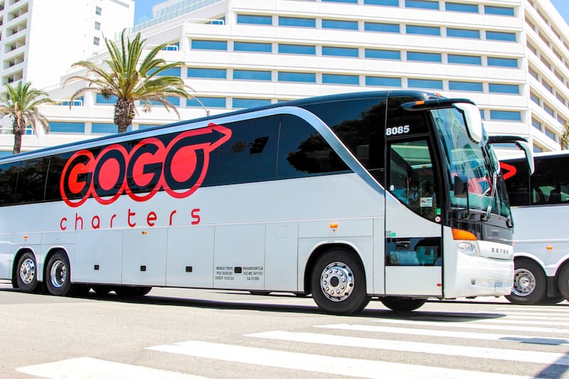 a white charter bus with the 'gogo charters' logo parked outside of a large building