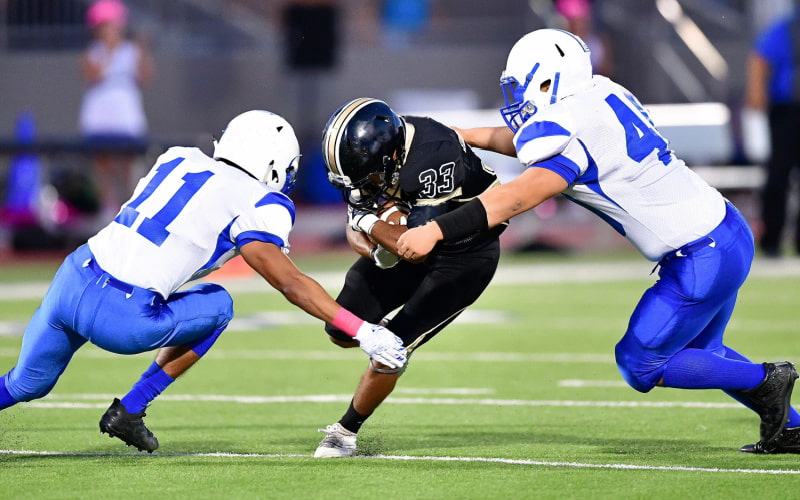 two football players in blue tackle an opponent