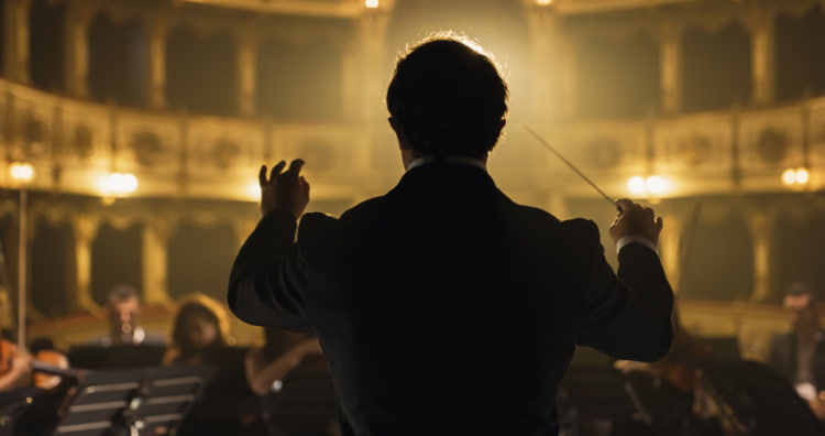 a conductor standing in front of an orchestra in a large concert hall