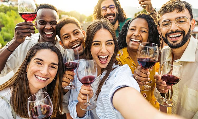 A group poses for a selfie, toasting wines of red wine at a vineyard