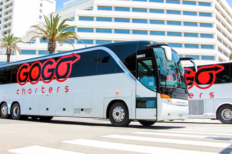 a white bus with a gogo charters logo, parked outside of a building with lots of windows