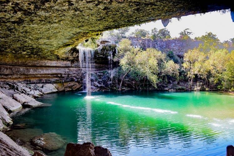 a waterfall and a blue pool of water at mckinney falls state park