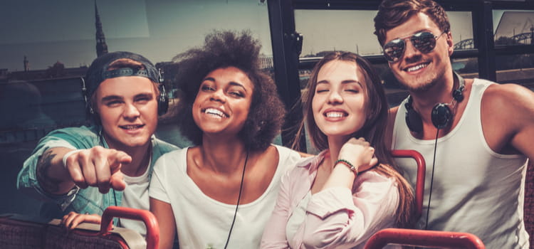 friends smile and point at the camera while on top of a tour bus