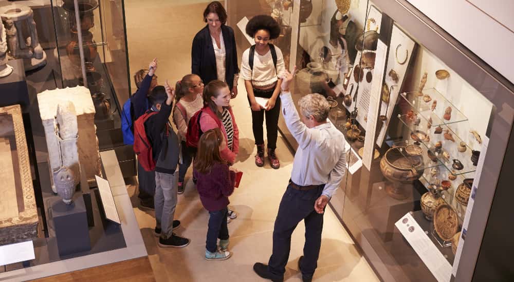 A class of students raise their hands during a museum field trip
