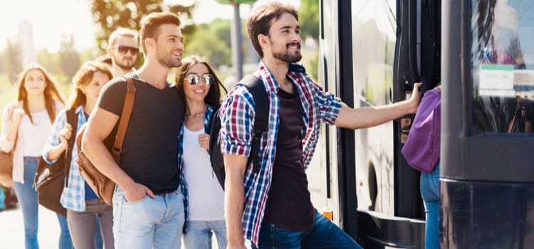 passengers smile as they load onto a charter bus on a sunny day