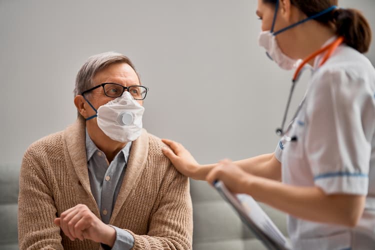 Nurse comforting old man, both wearing masks