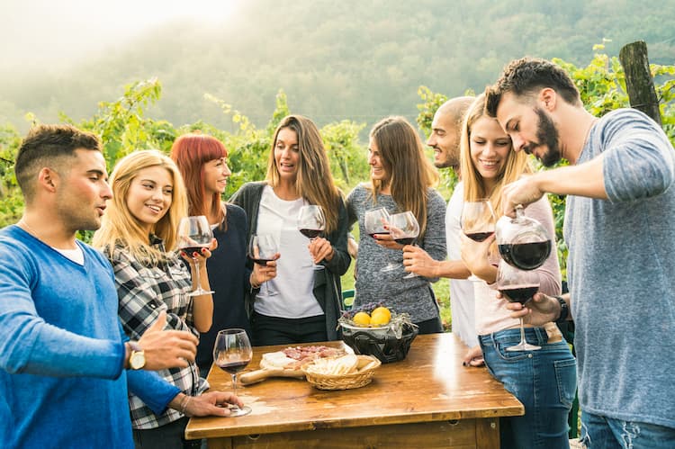 Large group of friends enjoying wine and food at a sunny vineyard and winery.