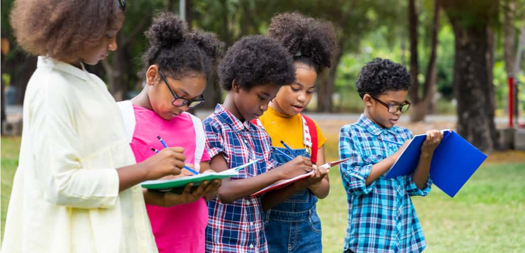 children writing in notebooks on a field trip