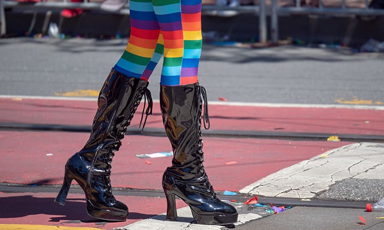 a person in rainbow tights and high heels walks on a street at San Francisco pride