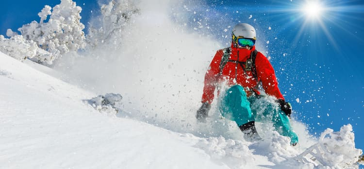 a skiier flies down the side of a snowy mountain, with snow clouds puffing up in the background