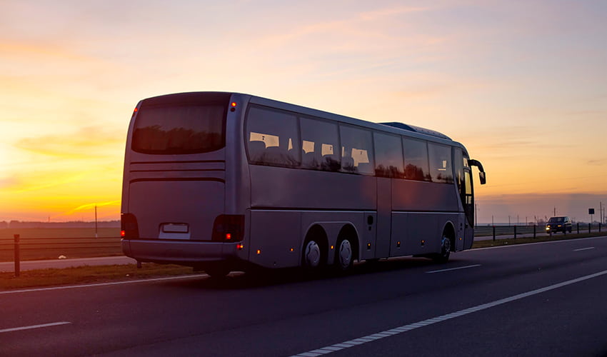 A charter bus drives on an empty road at sunset