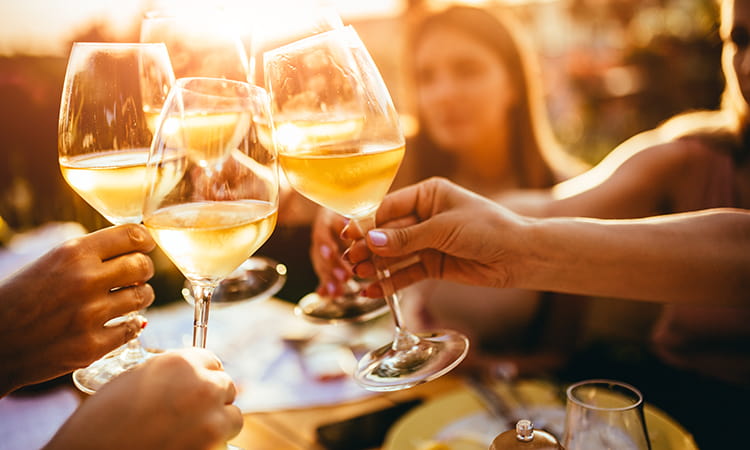 a group toasts glasses of white wine at sunset