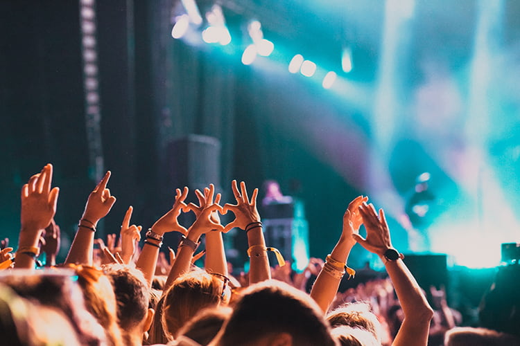 A crowd at a large concert cheers with their hands up
