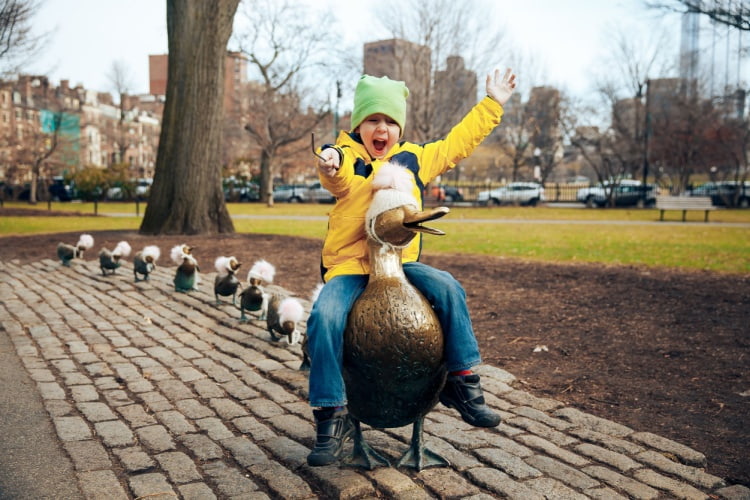 a child poses on a duck statue in boston