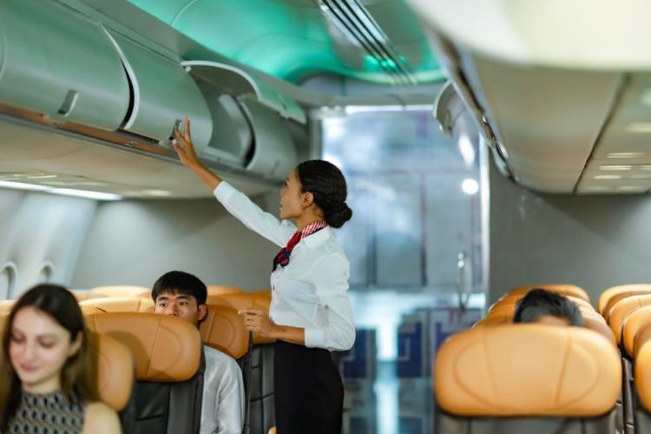 a flight attendant closes a luggage bin above a passenger's seat