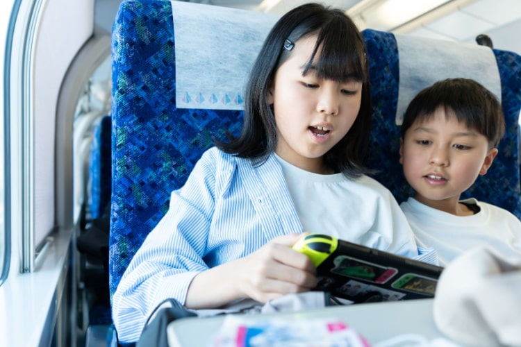 two children sit together on a charter bus playing on a gaming device