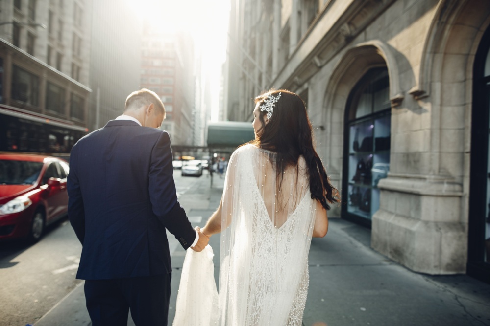 A bride and groom face away from the camera while walking through downtown Chicago