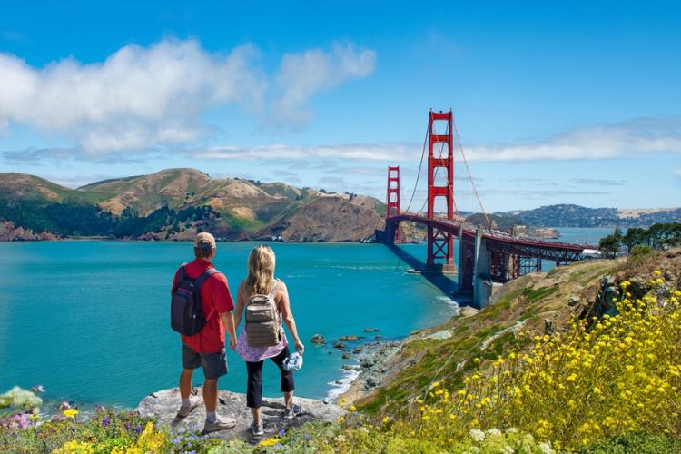 Two tourists stand on a vista point enjoying the view of the Golden Gate Bridge