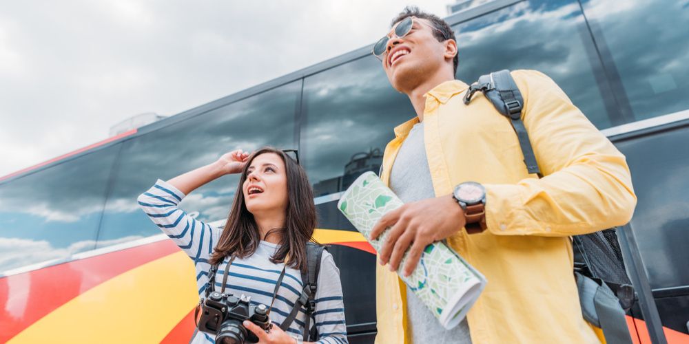 Two tourists standing outside of their tour bus and looking at an attraction