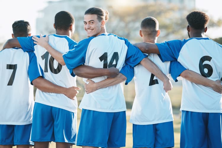 teammates in blue jerseys lock arms while one teammate looks back and smiles