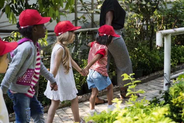 students hold hands while walking through a garden on a field trip