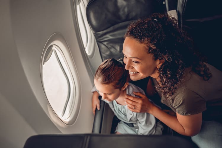 a mom and her child smile while looking out the window of a plane