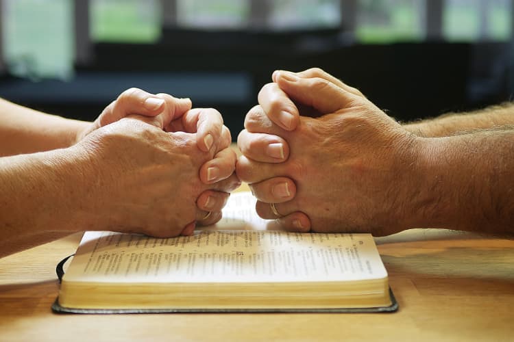 two people sit across from each other and fold their hands to pray