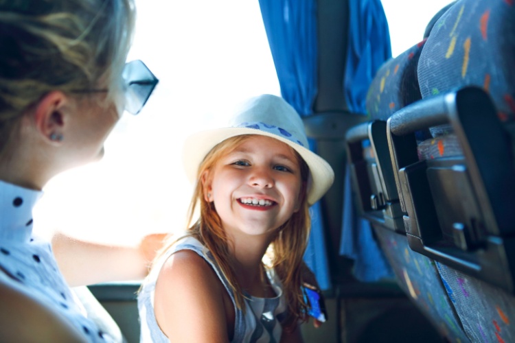 a child smiles at her mother while sitting on a charter bus
