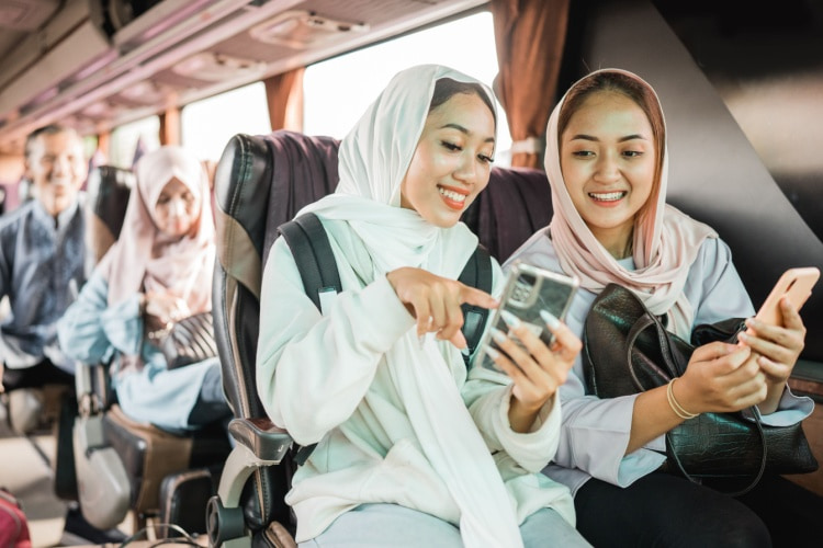 two women on a charter bus watch a video on a phone together