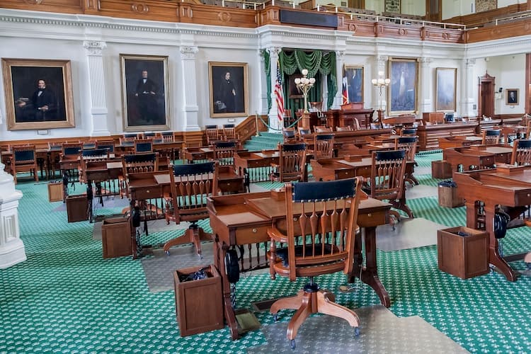 a gathering space inside the texas state capitol, with wooden chairs and green carpet