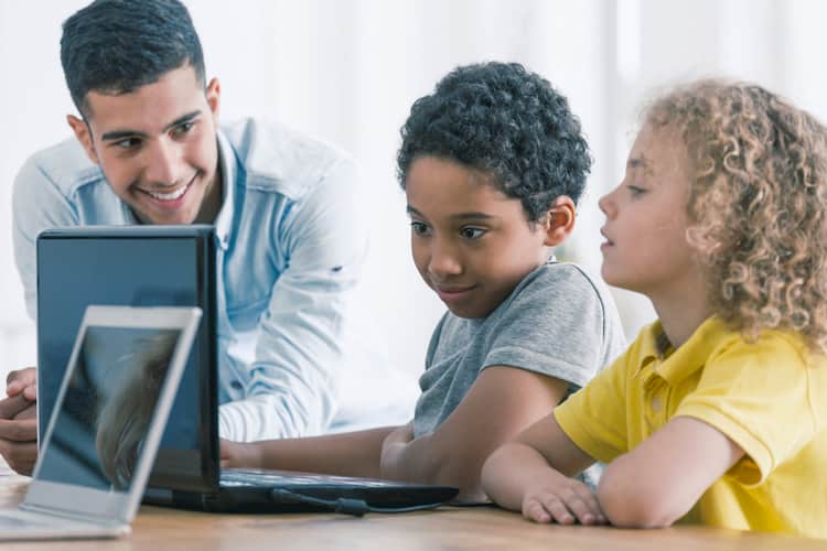 Young male teacher helping two students work on the computer